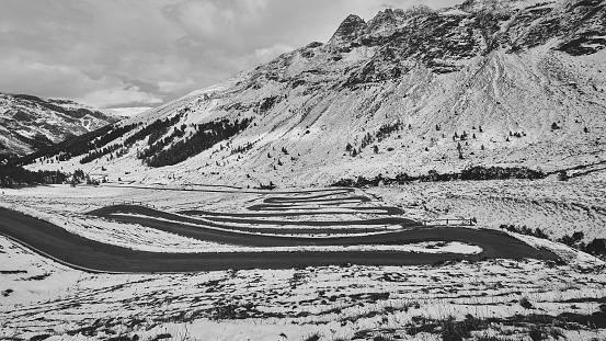 A grayscale shot of a landscape with a curvy road and a mountain in winter
