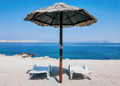 A vertical shot of an umbrella and chairs on the seashore against a blue sky backgrou