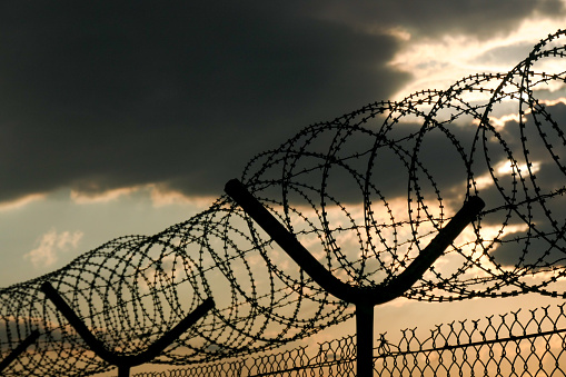 Storm clouds pass over the razor wire, barbed wire and wire mesh fences surrounding Sydney Kingsford-Smith Airport.   This image was taken from near Shep's Mound, a public viewing area off Ross Smith Avenue, at sunset on 10 February 2023.