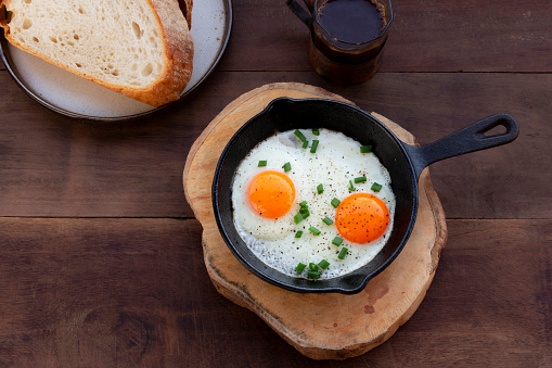 Fried egg in skillet pan isolated on wood background close up, top view, breakfast food concept.
