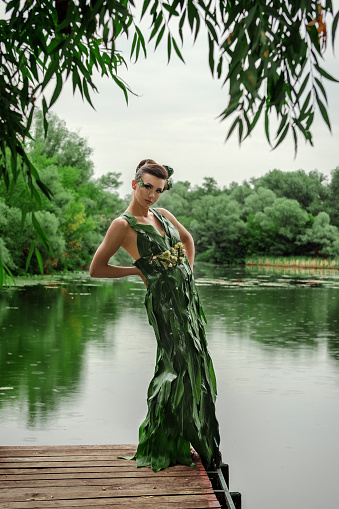 girl in a dress of green palm leaves on a forest lake