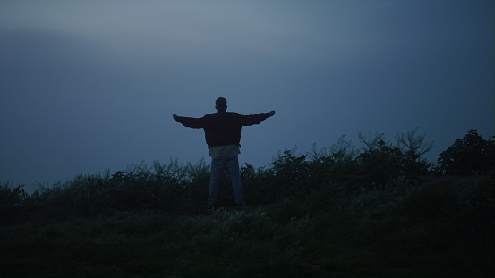 Lonely guy walking in misty field. Back view man raising hands in air. Positive male model enjoying freedom outdoors. Peaceful man looking mountain landscape in morning. Mysterious foggy atmosphere