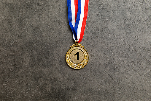 Simply flat lay design winner or champion gold trophy medal on concrete stone grey background. Victory first place of competition. Winning or success concept. Top view flat lay copy space