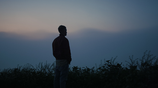 Peaceful man enjoying foggy landscape in morning. Depressed guy silhouette standing on mountain at sunrise. Sad man looking mystic horizon in autumn. Male person feeling harmony with nature alone