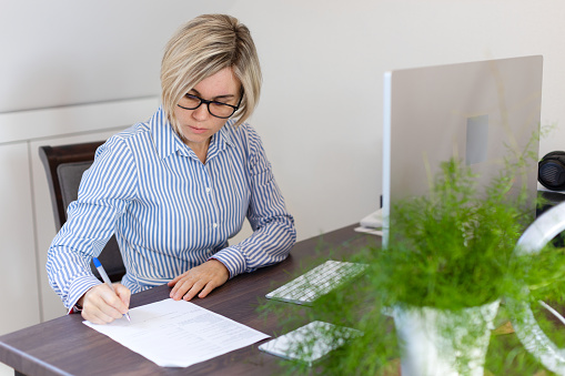 Business woman in glasses fills out paperwork and works in a computer. A woman works in the office or at home in the office. Business, work, documents, director