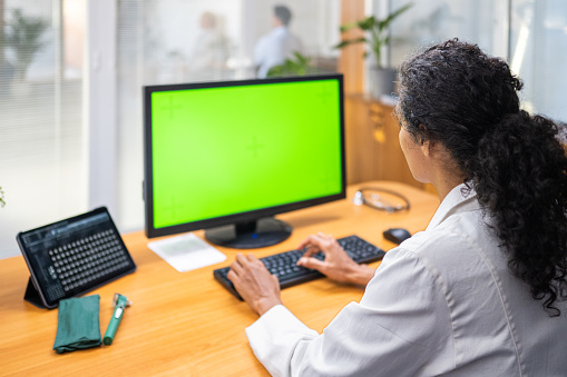 Rear view of hispanic female radiologist analysing patients MRI scan on green screen desktop.