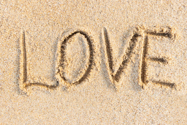 Love word written on sunny sand, textured beach background