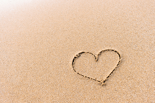 Heart sigh handwritten on sandy beach background with space for text