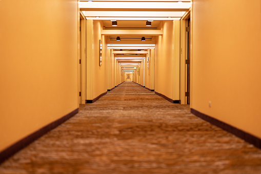 Long hotel corridor, hallway, with doors, carpet and yellowish beige tone.