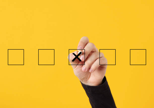 Rejection, cancellation, decline, wrong decision or choice concept. Male hand draws a cross x symbol in the middle of checkboxes on yellow background.