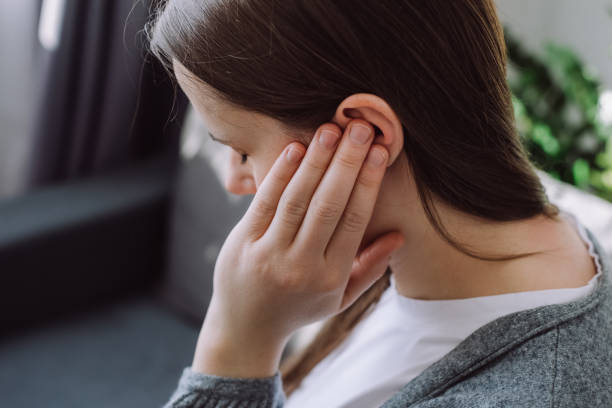Tinnitus concept. Close up up of sick young caucasian female touch plug ear suffer from noisy disturbing sound sitting on sofa at home. Annoyed millennial lady having earache, hearing problems stock photo