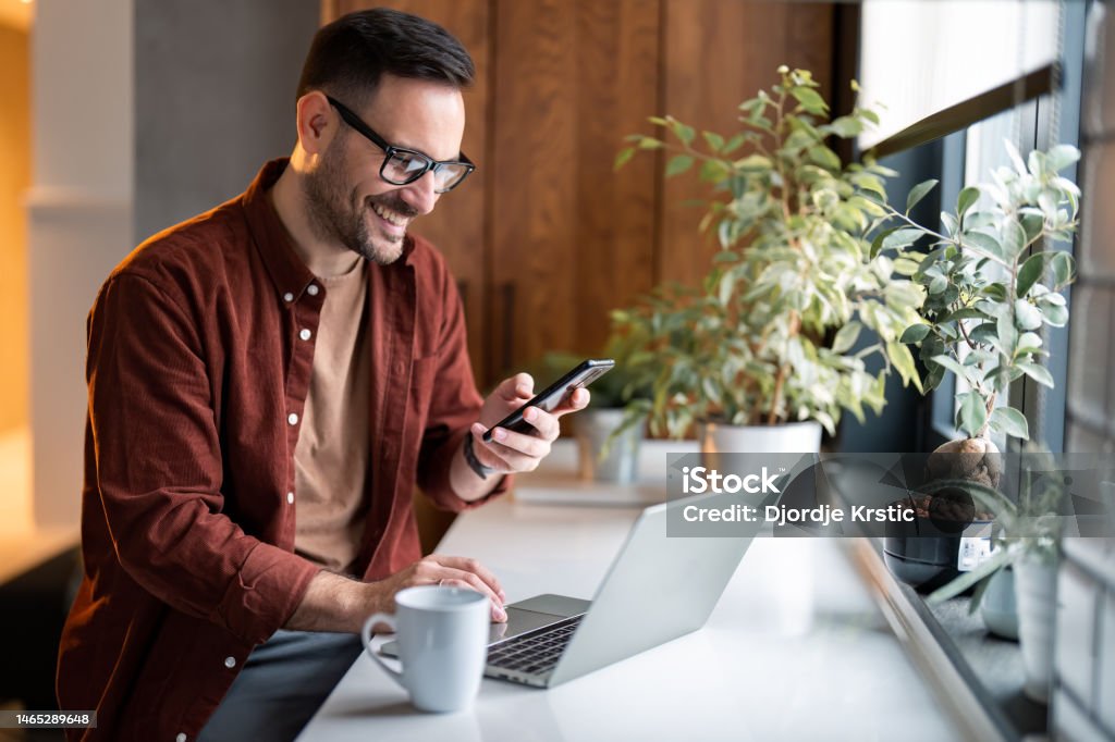 Satisfied modern millennial man in stylish casual clothes using smartphone and laptop computer - Royalty-free Telefoon gebruiken Stockfoto Satisfied modern millennial man in stylish casual clothes using smartphone and laptop computer - Royalty-free Telefoon gebruiken Stockfoto