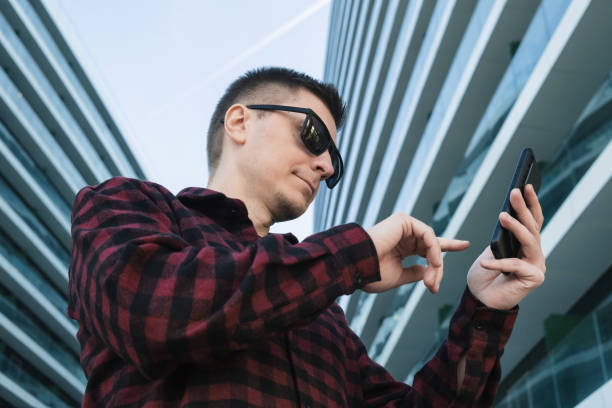 istock Young man freelancer or IT specialist in sunglasses using mobile phone or smartphone device outside 1465289652