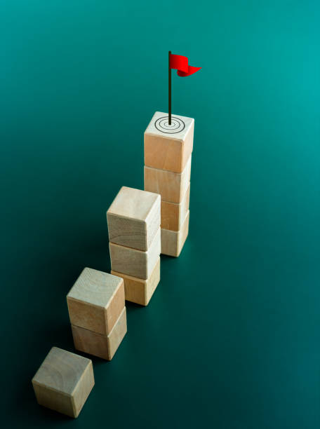 Red flag, the goal, target symbol on the top of wooden cube blocks, bar graph chart steps on green background. Business growth process, technology trend, mission to success concepts, vertical style. bandera roja, el objetivo, símbolo de objetivo en la parte superior de los bloques de cubo de madera, pasos del gráfico de barras sobre fondo verde. proceso de crecimiento empresarial, tendencia tecnológica, conceptos de misión al éxito, estilo vertic