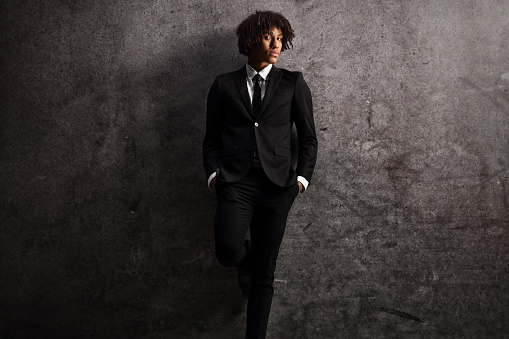 Young african american male model in a suit and tie leaning on a dark rusty wall