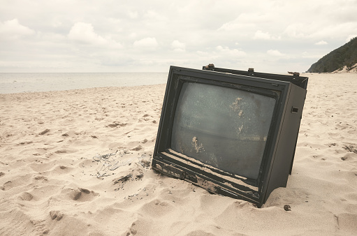 Old broken TV set on a beach, color toning applied.