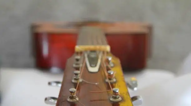 A macro and background of guitar strings on a wooden guitar. A used guitar, worn in, made good use of.