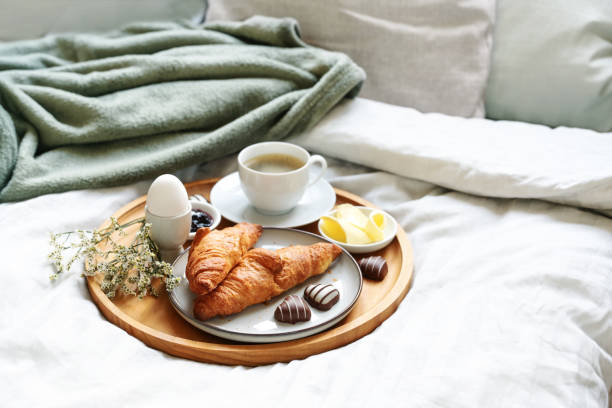 Mothers day breakfast served with love on bed. Coffee, croissant, egg and chocolate hearts on a wooden tray. Natural bed cloth. Also for birthday, valentines or fathers day, copy space stock photo
