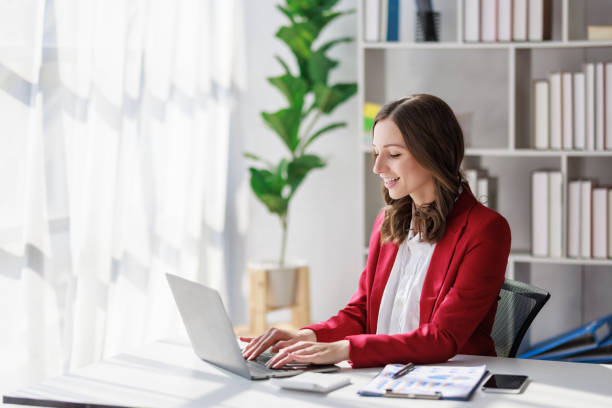 istock Concept of business working, Businesswoman wearing red suite smiling while using computer laptop for checking business analytic document  report  in her workstation. 1465307937