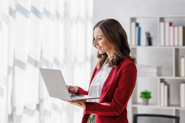 istock Concept of business working, Businesswoman wearing red suite standing while using computer laptop for checking business analytic document  report  with coffee cup on desk in her workstation. 1465307967