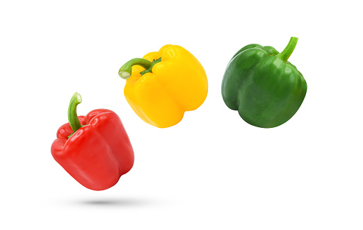 Three red, yellow, green bell peppers falling in the air isolated on white background.