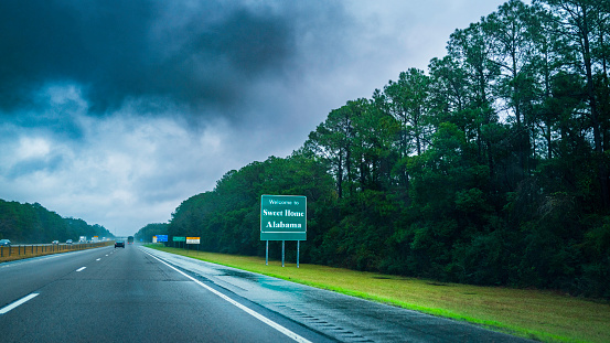 Welcome to Alabama Road Sign amd dramatic winter weather conditions and cloudscape on I-10 highway, passenger seat road trip snapshot