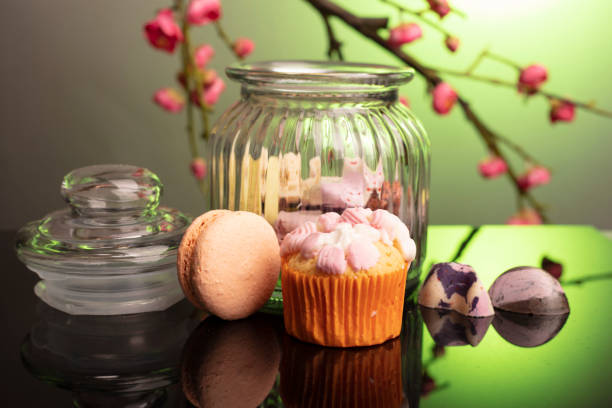 A red cookie jar filled with mini muffins is surrounded by individual muffins scattered across a distressed white wooden table, creating a playful and informal Valentine’s Day snack scene. The bright, airy background provides ample copy space on the left and top for text overlays, banners or social posts, while the golden pastries and long shadows add warmth and a relaxed, homely mood.