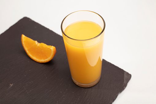 Front view of orange fruit and glass of orange juice on black background.