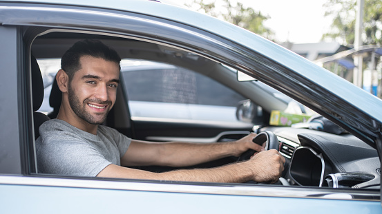 Happy man driving a car and smiling. Cute young Hispanic male success happy brunette. Portrait of happy driver steering car Holiday.
