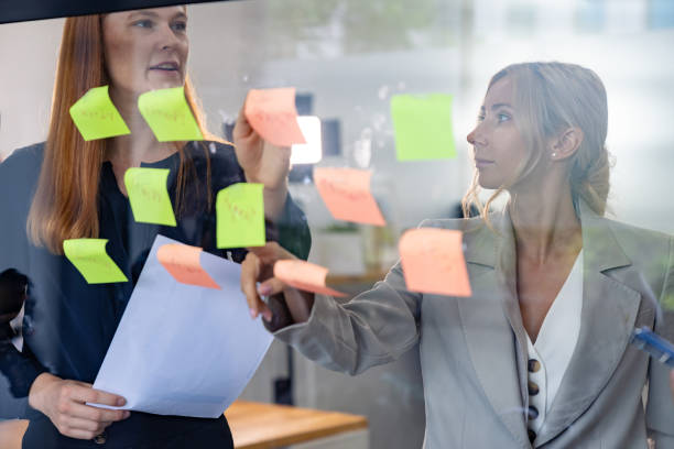 istock Group of businesspeople brainstorming and writing strategy ideas in post it notes or sticky note on glass wall in office 1465316357