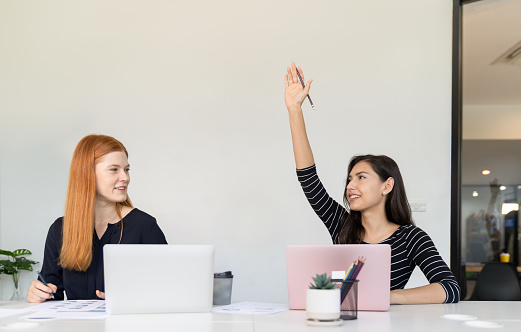 Businesswoman raising her hand and asking questions while meeting with colleague in office.Young woman use laptop and share idea with business team.