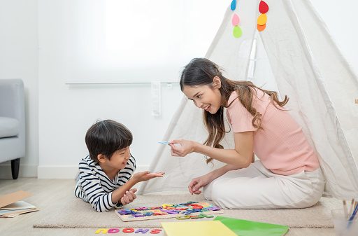 Mother and little son playing alphabet toys together on floor with play tent for children in living room at home