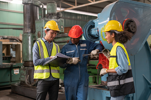 Male and female engineers in safety vest with helmet look at machine specification documents for repair and maintenance at industry manufacturing factory