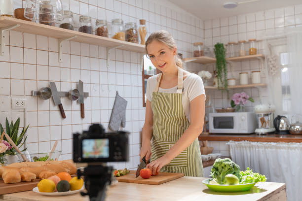 istock Young beautiful woman using camera recording video how to make a salad and making bakery for posting to social media in her channel food healthy at home kitchen 1465317184