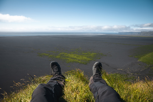 Tourist laying in a grass on top of the cliff and watching towards the sea in South coast of Iceland.