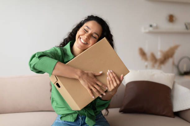 Contented Woman Buyer Hugging Cardboard Box Sitting At Home stock photo