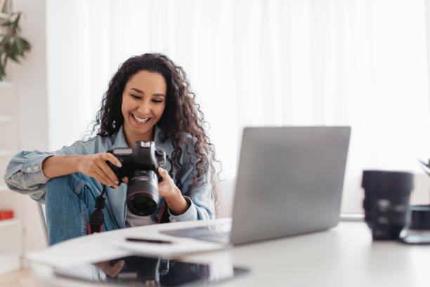 istock Joyful Professional Photographer Lady Holding Camera Using Laptop At Workplace 1465326311