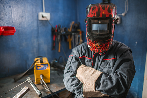 A welder with protective gloves and a welding helmet is welding in a metal workshop