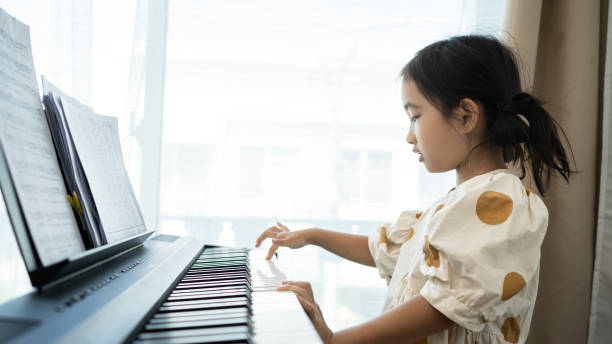 little asian cute girl playing the piano at home. home lesson on music for the girl on the piano. - child prodigy imagens e fotografias de stock