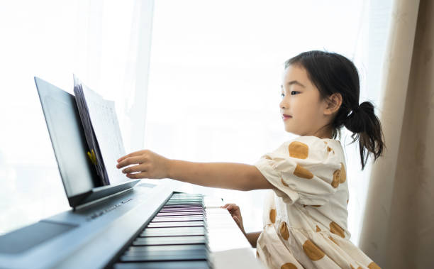 little asian cute girl playing the piano at home. home lesson on music for the girl on the piano. - child prodigy imagens e fotografias de stock