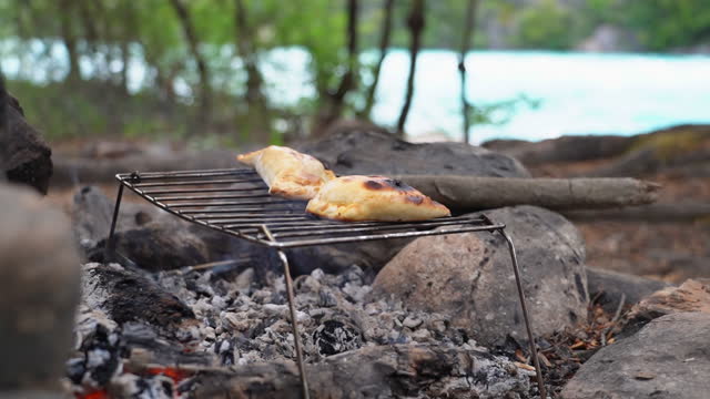Empanadas being heated up over open flame camp fire next to Rio Baker with white water rapids and turquoise water along the Carretera Austral, Patagonia, Chile, South America