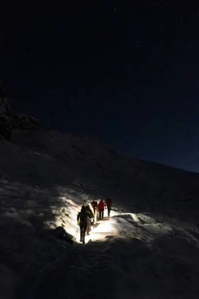 Hikers climbing the mountain at night with headlamps to see a sunrise in the mountains. Picture taken in the Bavarian Alps, in the first hours of the morning, with snow and a starry night with many stars.