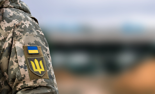 Ukrainian soldier in the army and flag, coat of arms with a golden trident on a military uniform background. Armed Forces of Ukraine.