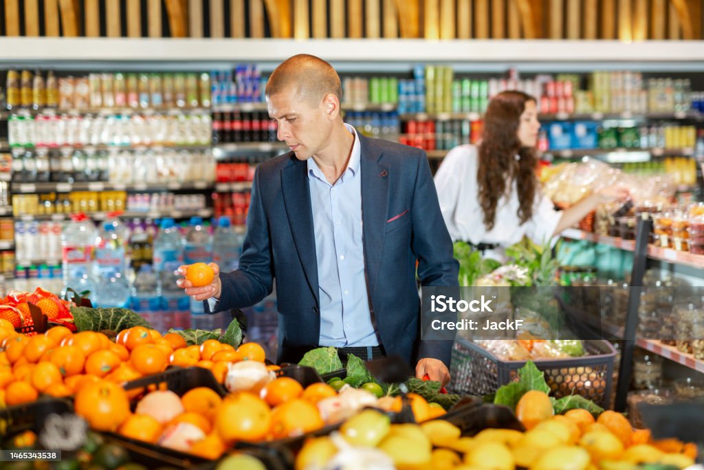 Young man carefully selects tangerines in the supermarket Young man carefully selects tangerines in the counter in the supermarket 18-19 Years Stock Photo