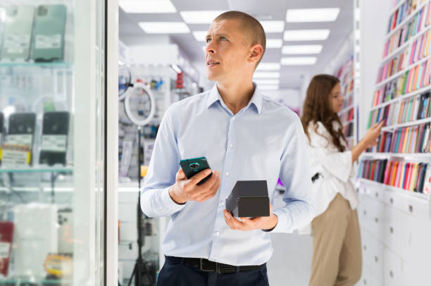 istock Smiling male holding mobile phone in the hand at electronics store 1465343652