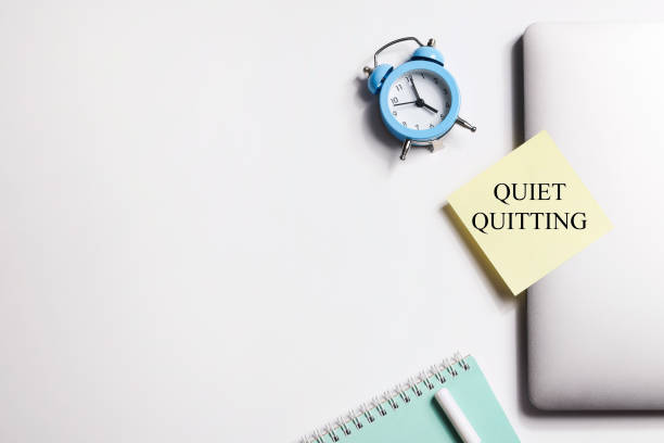 istock quote 'Quiet quitting' on yellow sticker on computer with clock and notebook. work life balance concept. post covid life philosophy. 1465344925