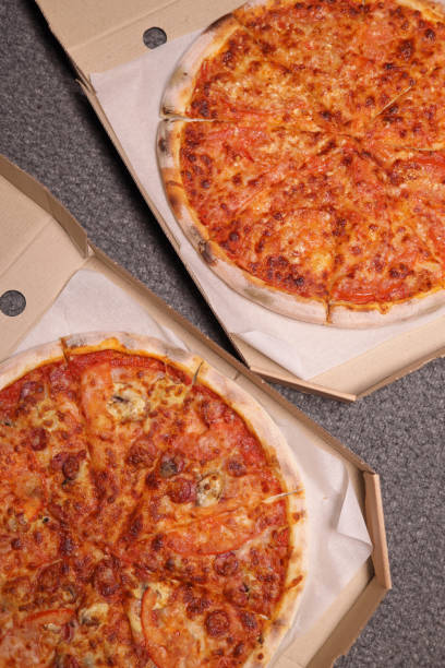 istock Whole pizzas with cheese, ham and tomatoes in a delivery box. Vertical Orientation 1465345418