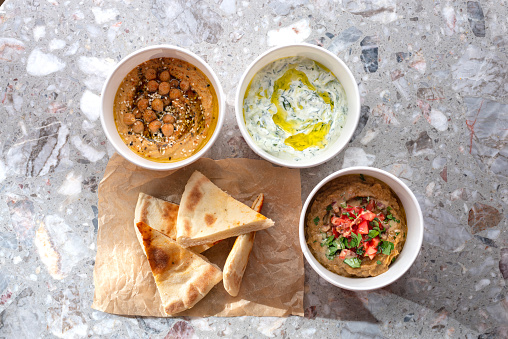 Pita with assorted traditional greek dips, tzatziki, vegetable caviar, hummus over light background. Top view, flat lay. Food for delivery. Fast food on the street