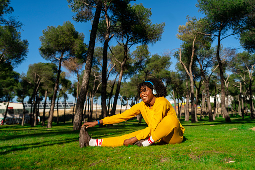 An Afro girl dressed in yellow tracksuit stretching before starting a run in the park.
