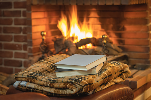 Books on top of a blanket in front of the cozy fire of the fireplace in winter